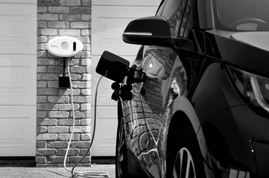 Black and white photo of an electric car being rapidly charged with BP pulse next to a garage door